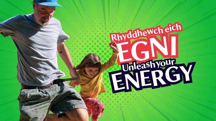 An adult and child jumping together on a green background with the words “Unleash your Energy" in English and Welsh